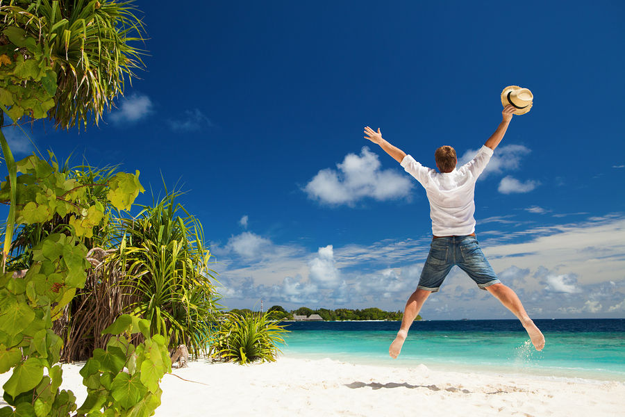Happy man jumping on the tropical beach. White sand, blue cloudy