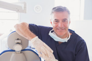 Smiling dentist leaning against dentists chair in dental clinic